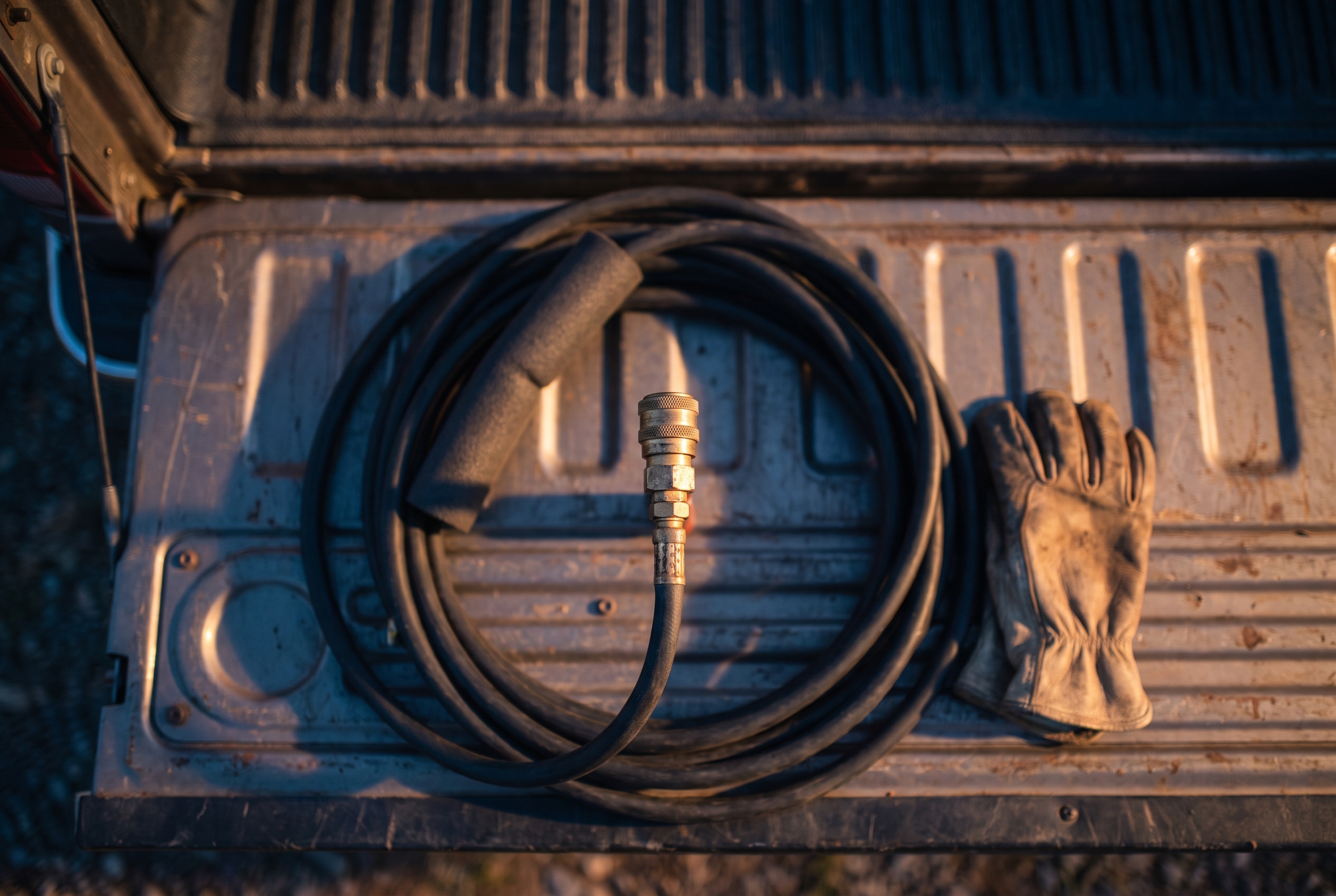 An overhead view of irrigation blowout tools including a compressor fitting, air hose and insulation sleeve laid out on a truck tailgate at dusk