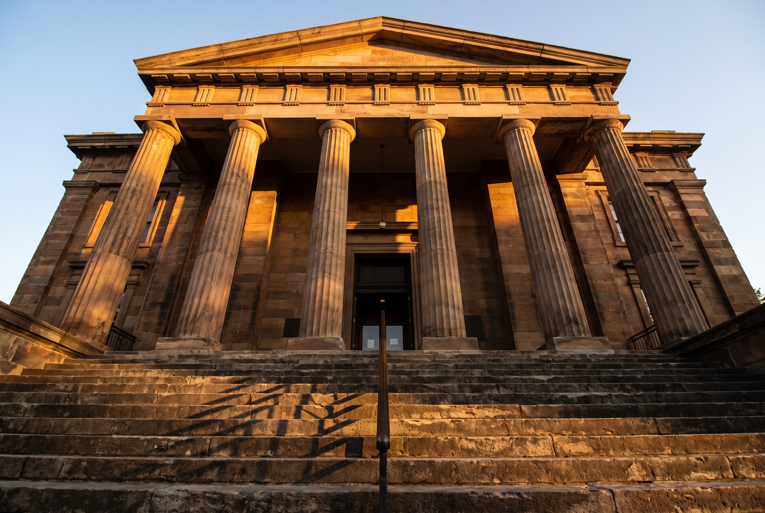 Stone courthouse columns and a wide staircase stretch upward under long shadows cast by late-afternoon sun.